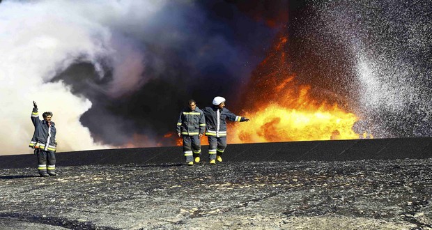 Firefighters walk near the fire of a storage oil tank at the port of Es Sider in Ras Lanuf